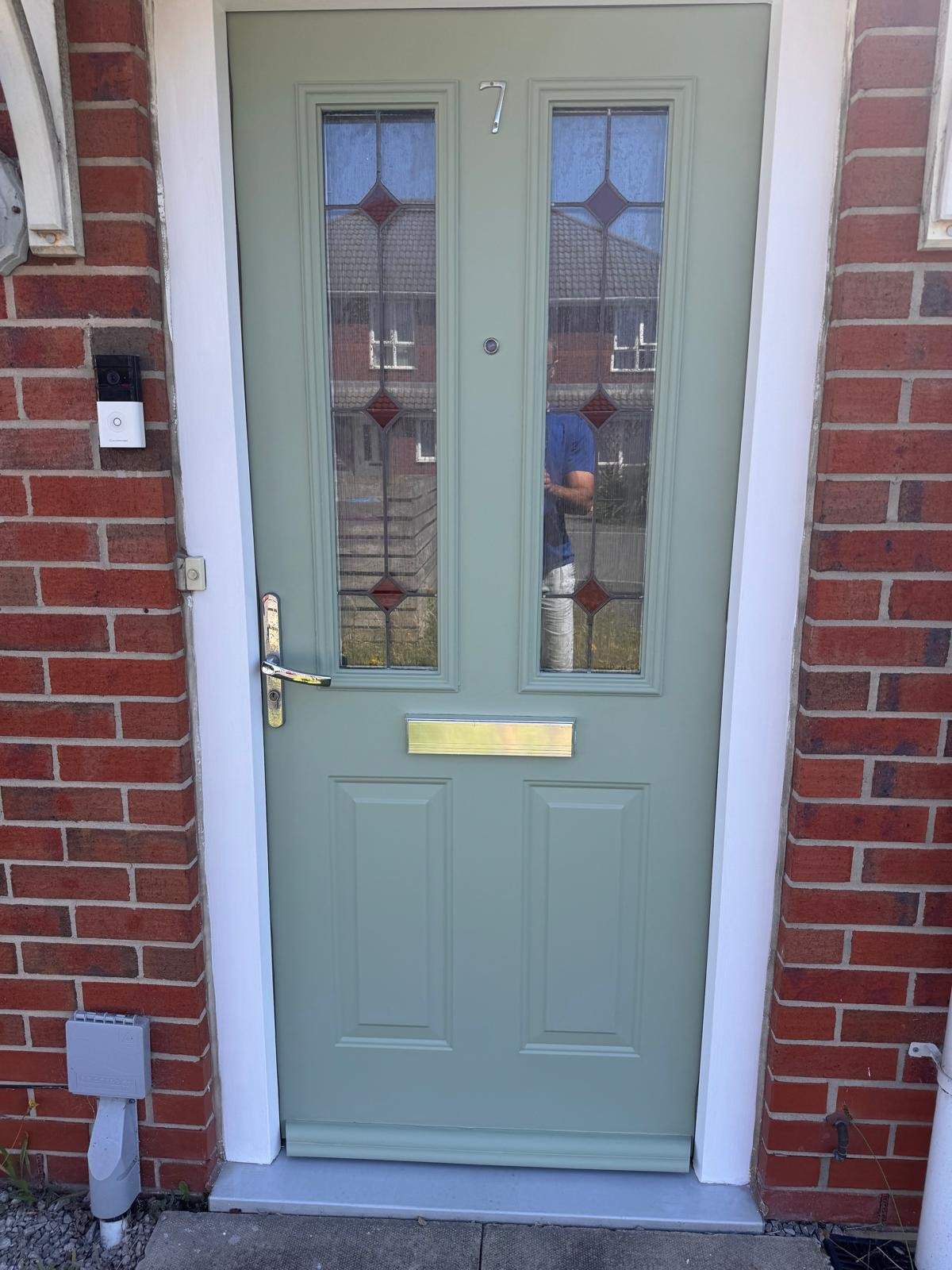 A sage green composite front door in a brick surround