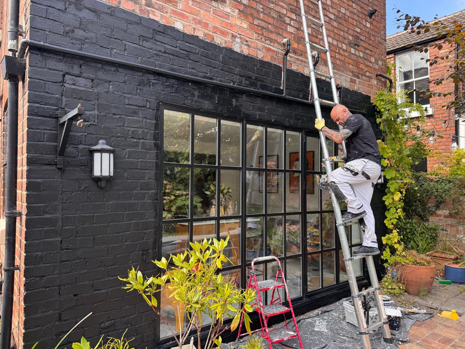 Black painted brick exterior with black window frames and a ladder in place