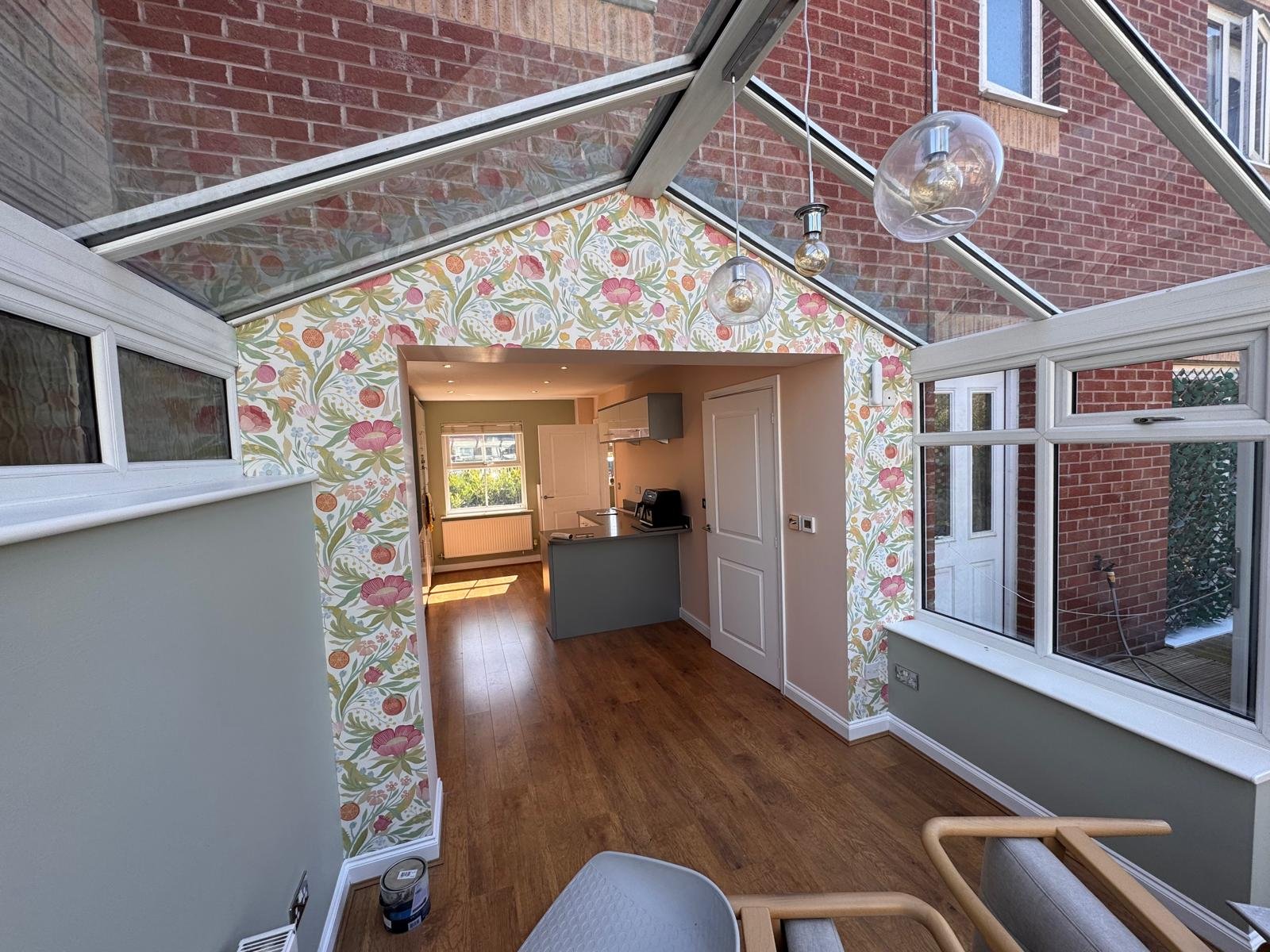 Glazed garden room with a floral papered arch through to a kitchen