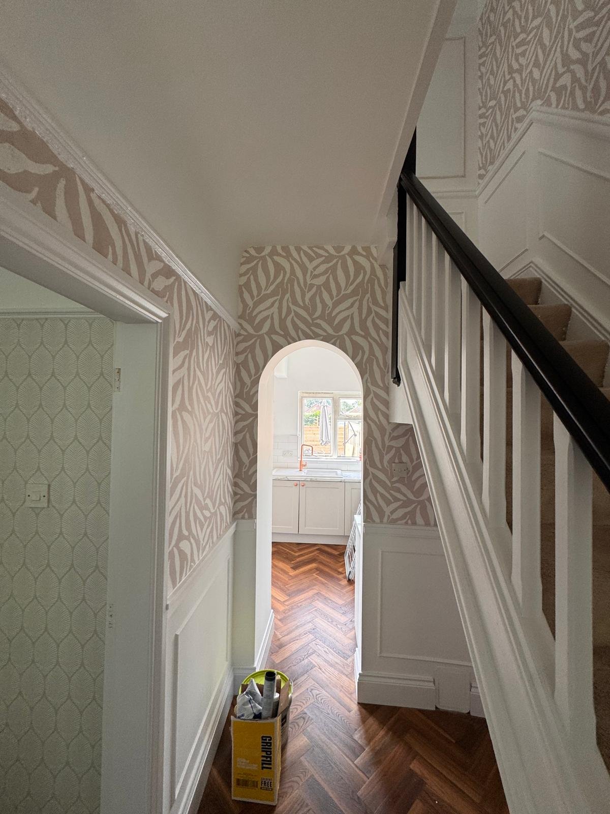 Hallway with leaf patterned wallpaper, white panelling and an arched opening
