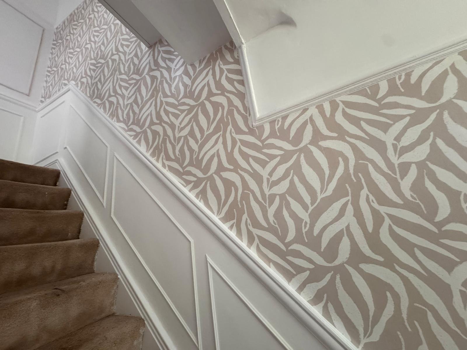 Staircase with leaf patterned wallpaper above white wall panelling