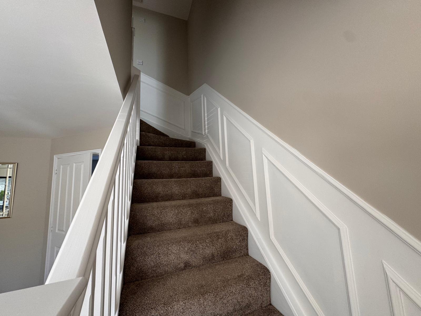 Staircase with white wall panelling and a painted handrail